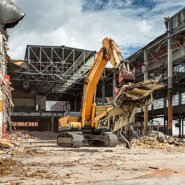 Heavy excavator demolishing reinforced concrete industrial process building