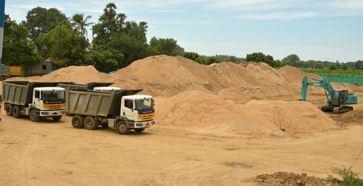 Loader and tipper trucks handling bulk construction sand at stockyard